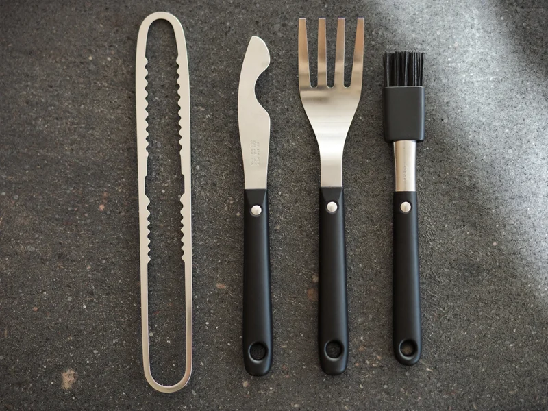 Edelstahl-Grillbesteck mit Zange, Wender, Gabel und Backpinsel auf dunkler Schieferplatte