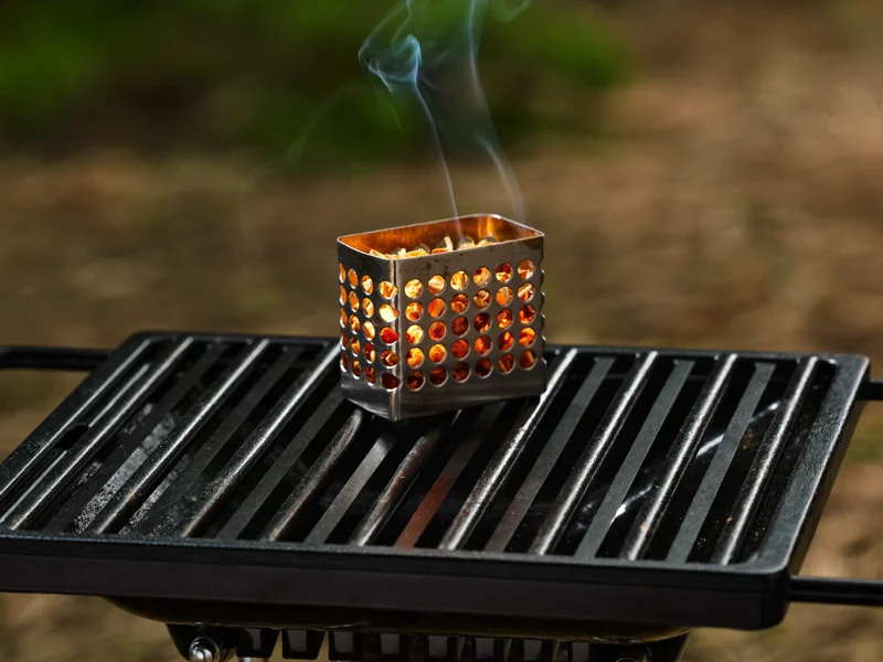 Gussrost und Raucherbox mit glühenden Holzspänen auf einem kompakten Tischgrill